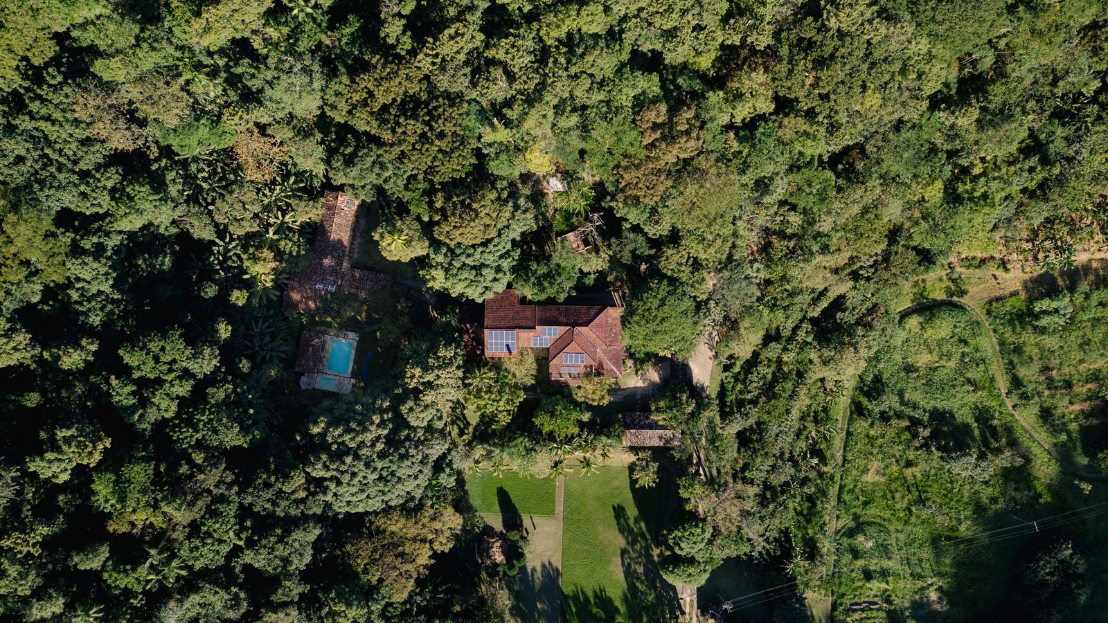 Vista aérea da Mata Atlântica preservada ao redor da fazenda, com telhados da casa entre as copas das árvores